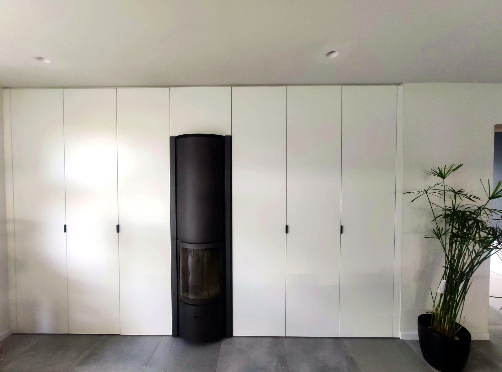 Moderne maatwerk garderobe kast met witte gesloten deuren en zwarte centrale haard in gerenoveerd interieur Oost-Vlaanderen.