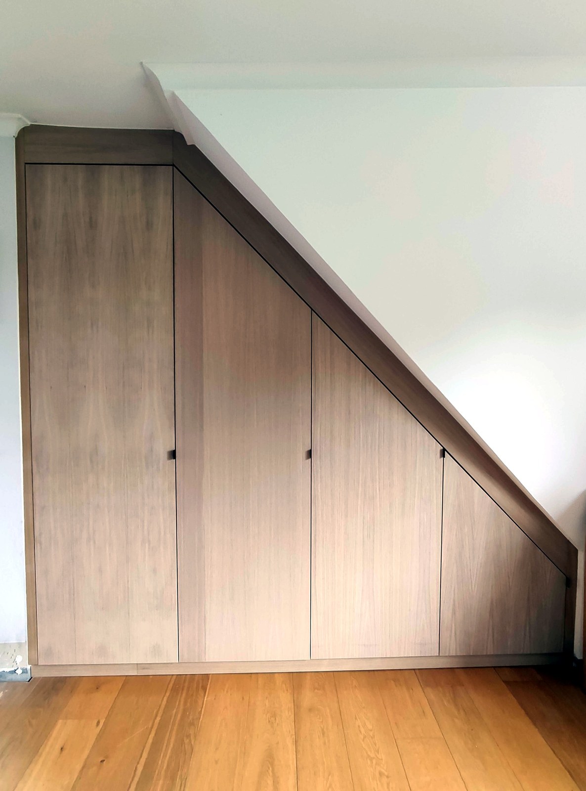 Maatwerk houten kasten onder schuine dak, moderne grijze schuifdeuren, professionele interieur renovatie in Oost-Vlaanderen