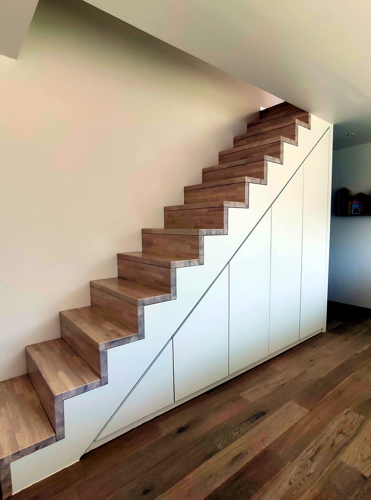 Moderne trappenhuis renovatie met op maat gemaakte houten trap en wit onderkastruimte in Oost-Vlaanderen.