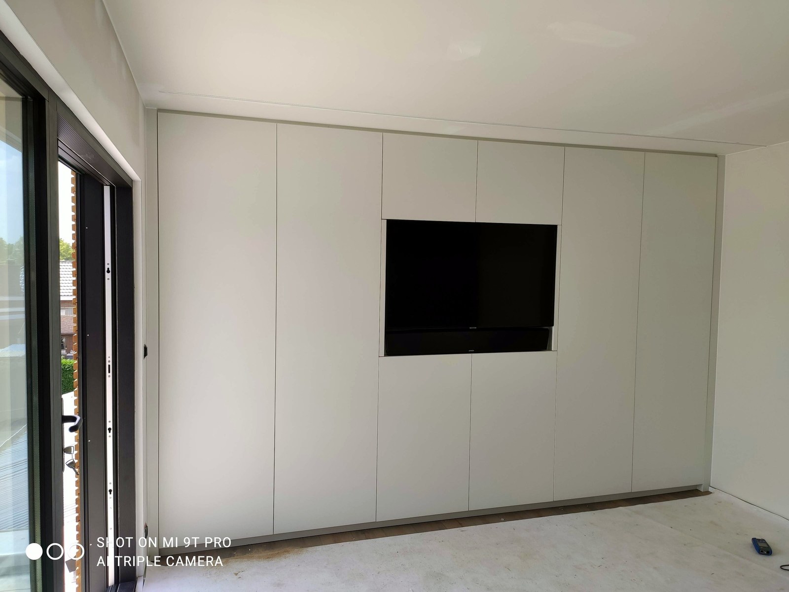 Moderne renovatie woonkamer met maatwerk wit gepanelde TV-muur en inbouwkasten, uitgevoerd door specialist in Oost-Vlaanderen