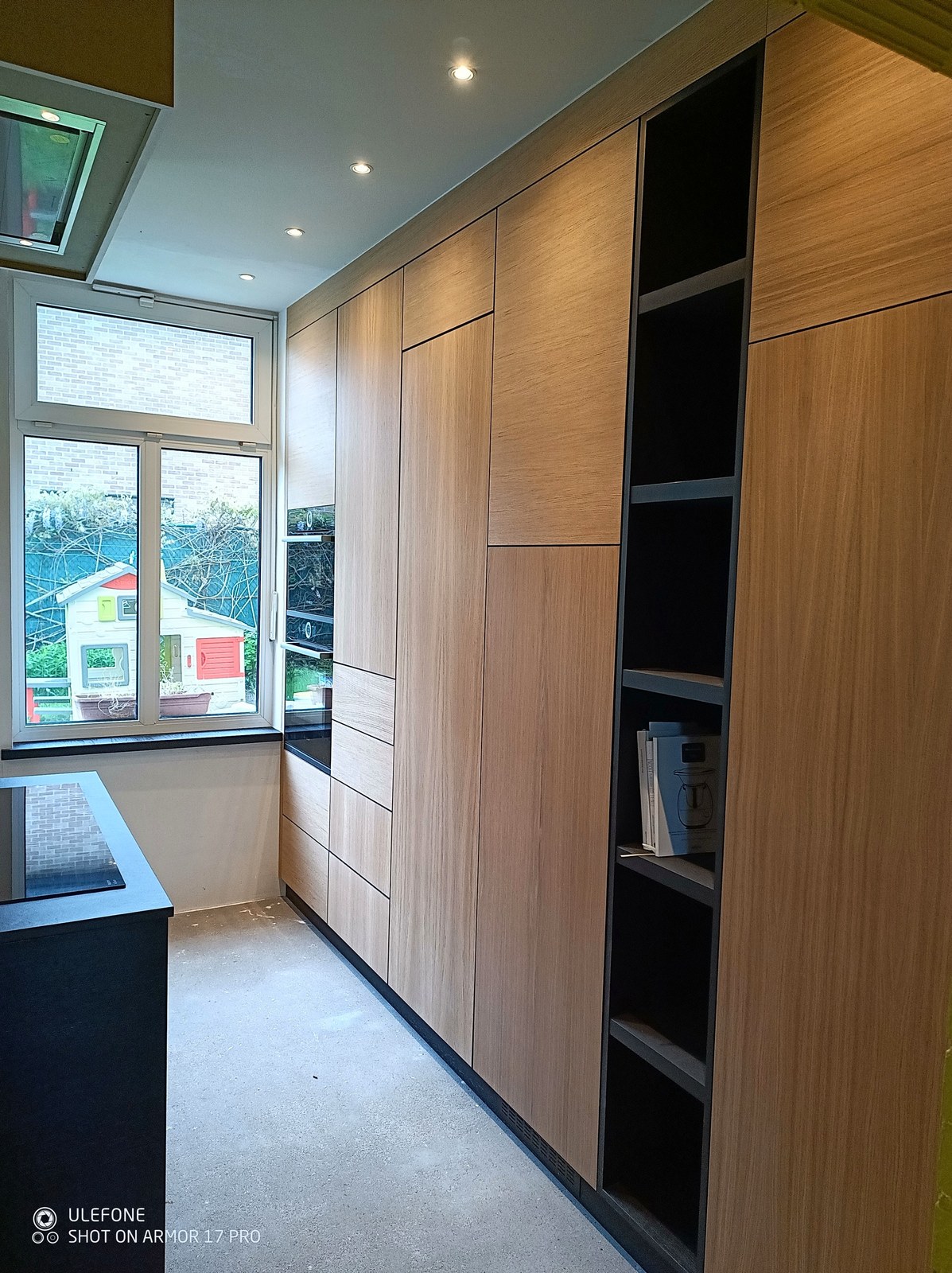 Moderne op maat gemaakte houten garderobekast in renovatie project Oost-Vlaanderen met elegante zwarte details en natuurlijke houttinten.